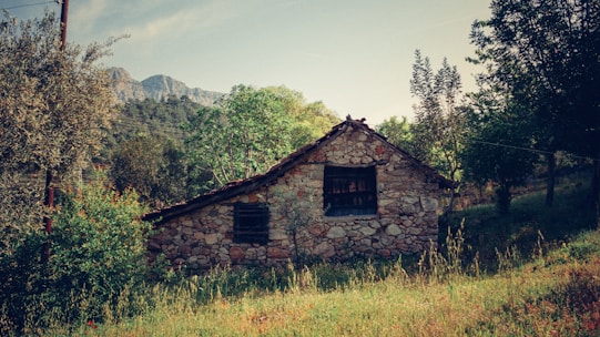 Cozy stone cottage nestled among rolling green hills under a bright blue sky.