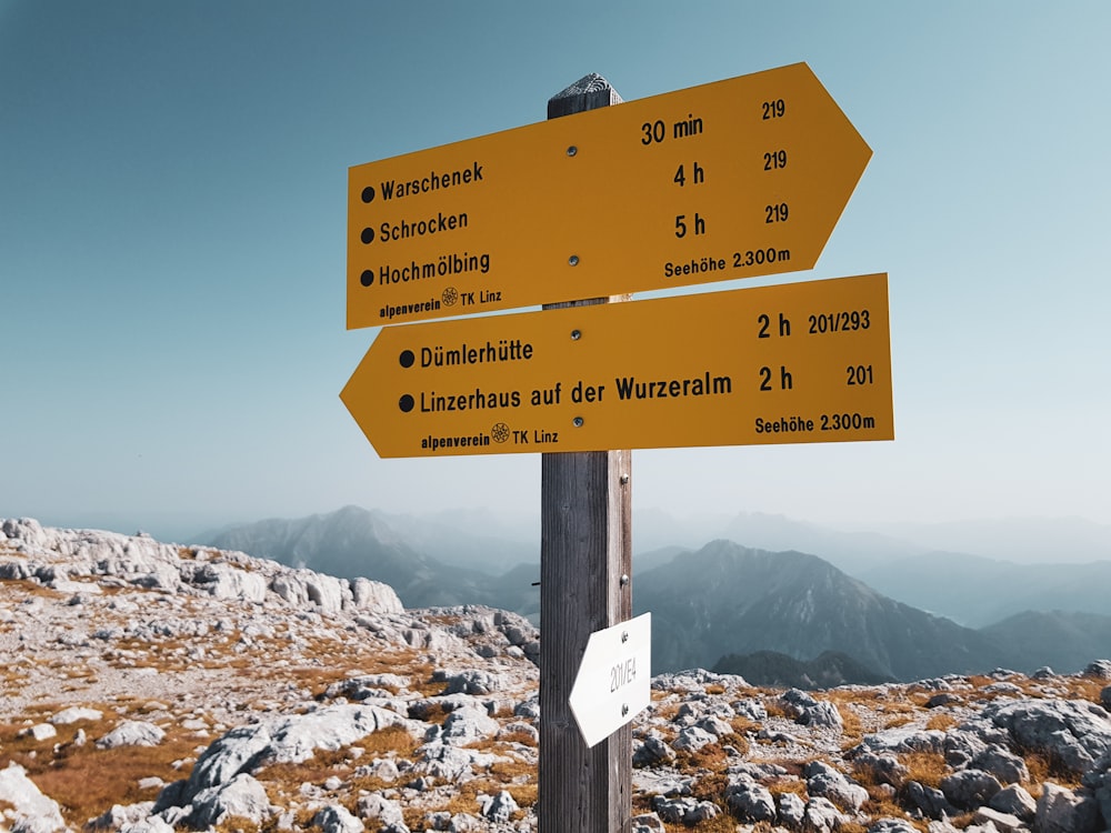 a yellow sign pointing in different directions on top of a mountain