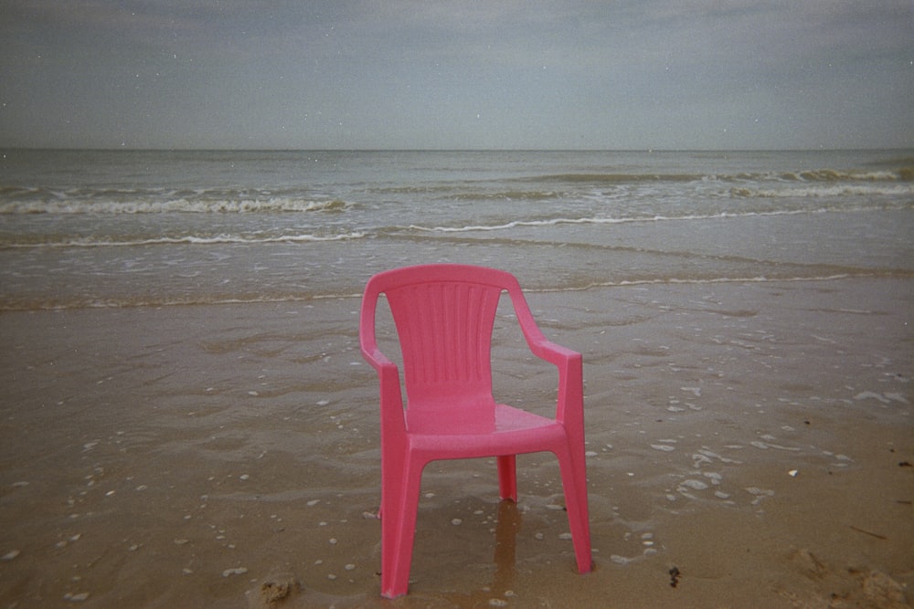 uma cadeira rosa sentada em cima de uma praia de areia