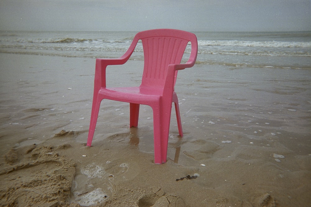 모래 해변 위에 앉아 있는 분홍색 플라스틱 의자