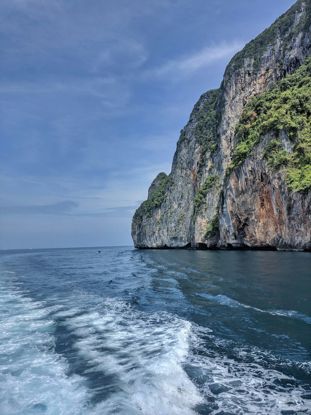 a boat traveling past a large mountain on a body of water