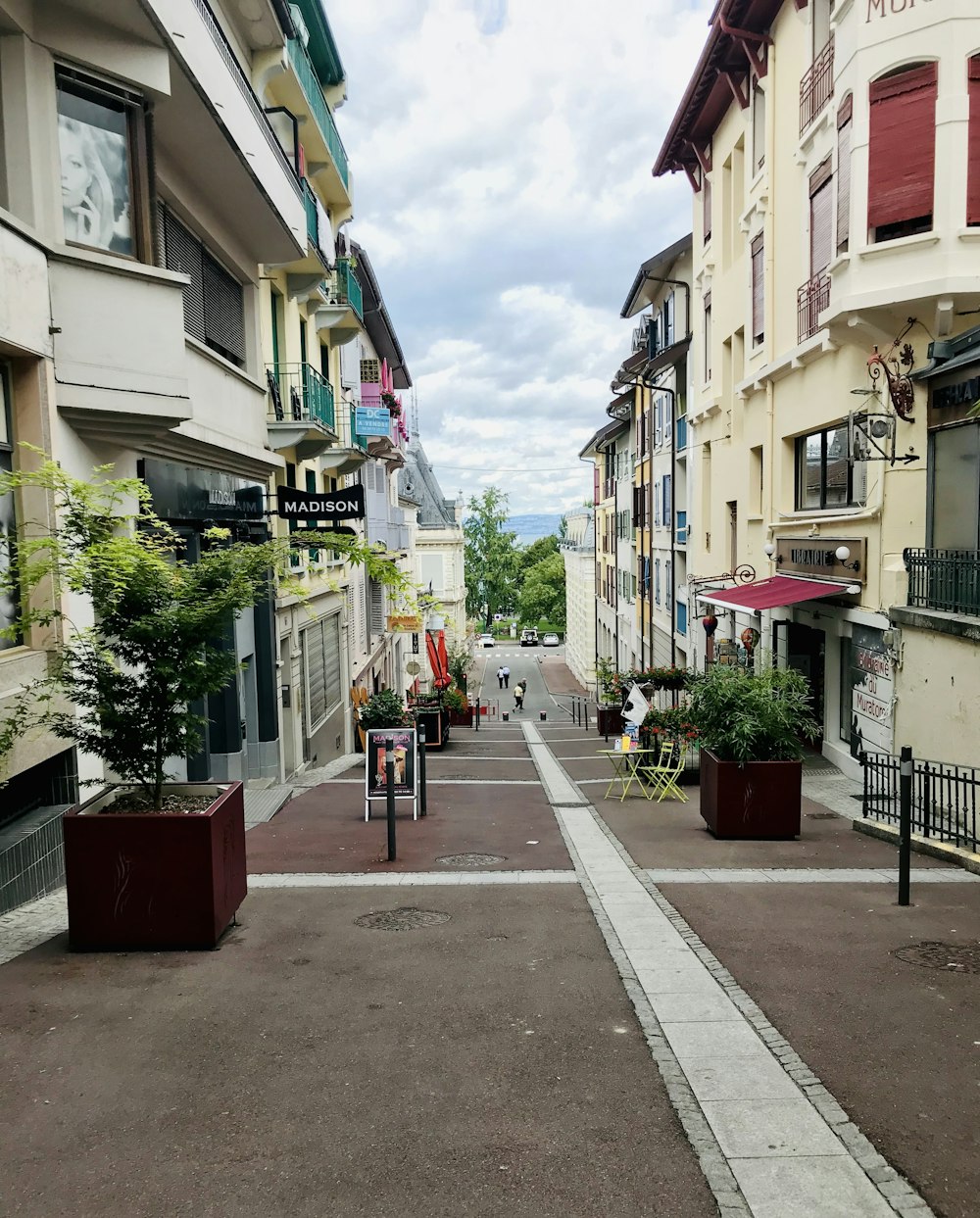 a narrow street lined with tall buildings and potted plants