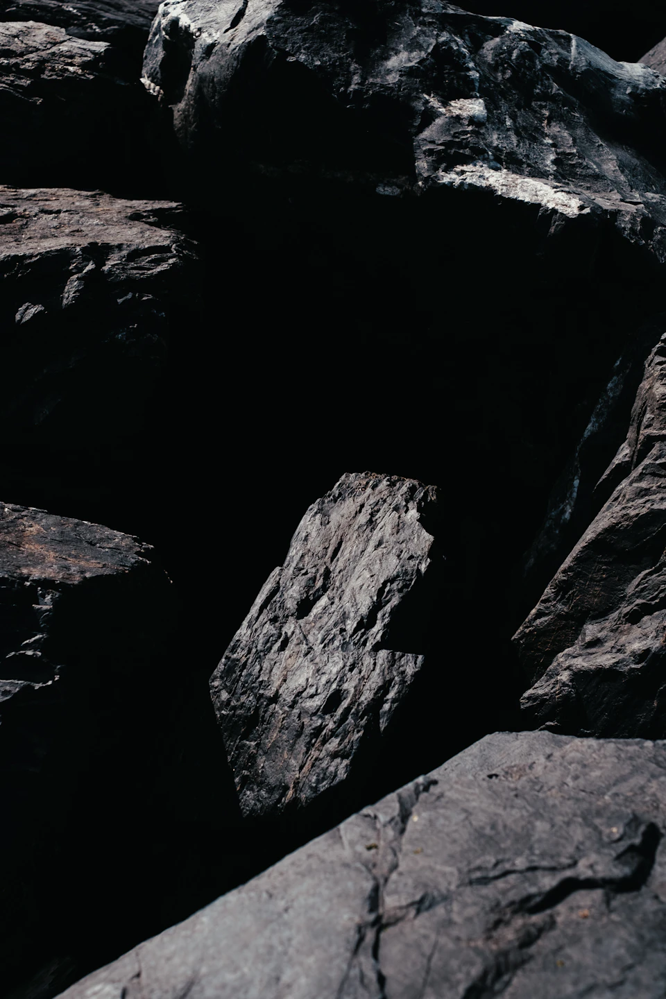 Dark gray rocks scattered across rocky landscape, some jagged, others smooth and reflective surfaces