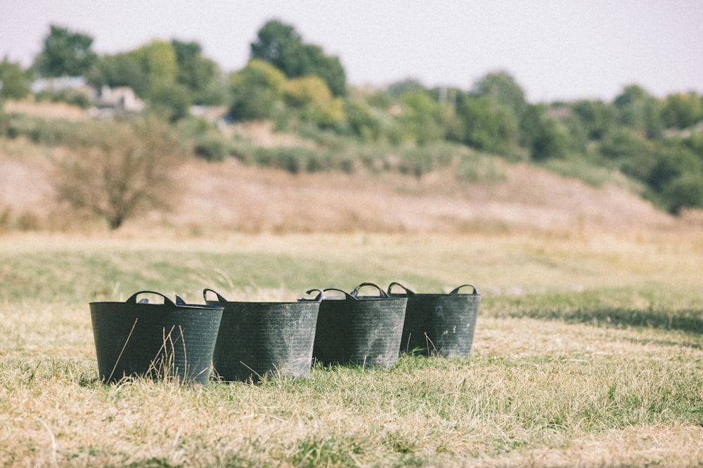 four black buckets sitting in the middle of a field