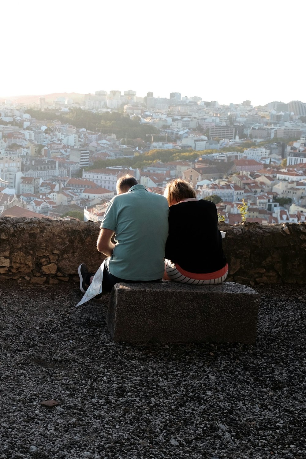 two people sitting on a stone bench overlooking a city