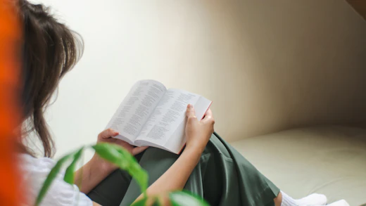 A woman reading a book beside a green plant