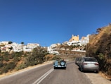 A winding Santorini road with a VIP van cruising under a bright blue sky