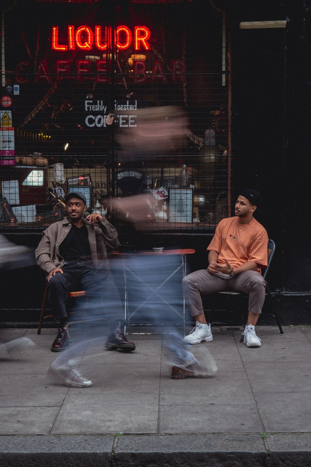 two men sitting on a bench in front of a liquor store