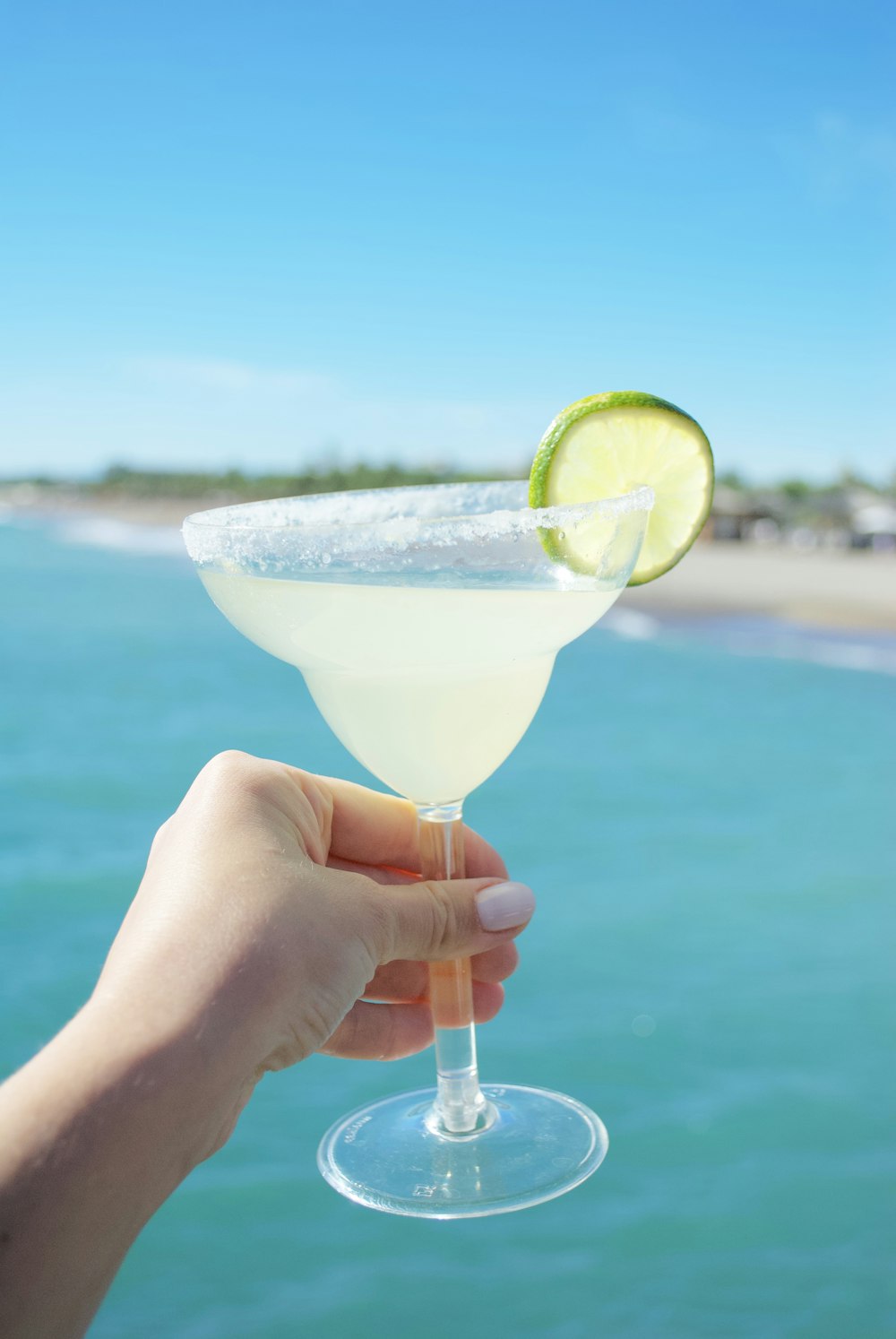 une main tenant un verre à martini avec une tranche de citron vert sur le bord