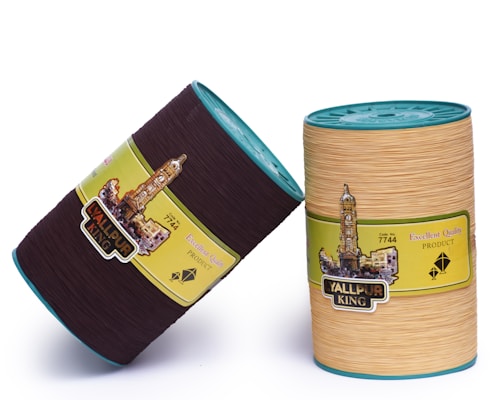 Two cylindrical containers with lids are displayed against a plain backdrop. The first container is dark brown, and the second is beige. Both have labels featuring an image of a clock tower and text, including 'Yallpur King' and 'Excellent Quality Product'. Each container has a turquoise lid.