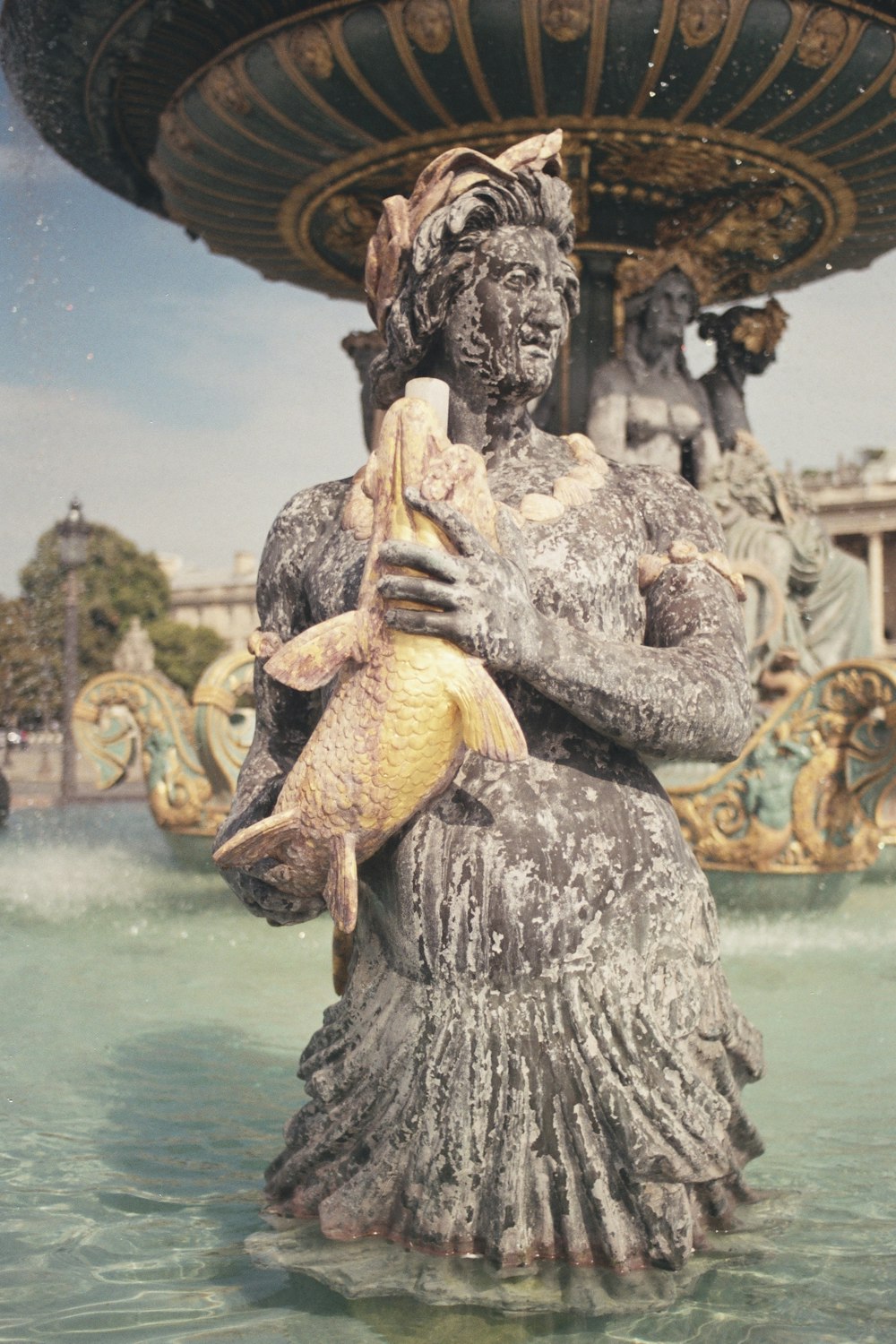 a statue of a woman holding a fish in front of a fountain