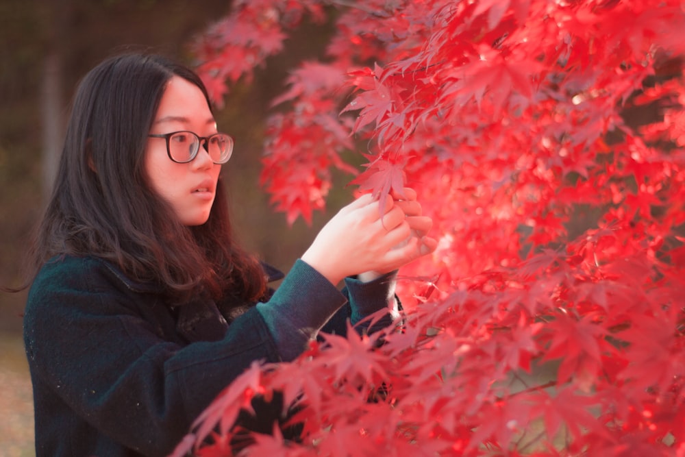 a woman in a black jacket and glasses holding onto a red tree