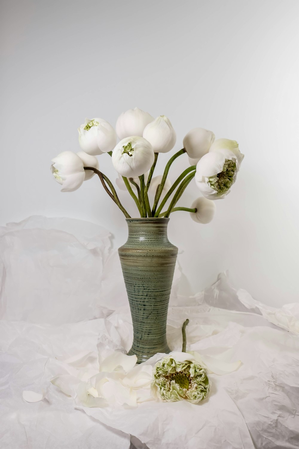 a green vase filled with white flowers on top of a table
