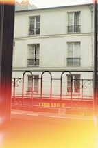 View of a typical Parisian building with multiple windows and intricate black wrought iron railings. The word 'LIBRAIRIE' in yellow letters is visible on a red storefront below. A light leak effect creates a warm, yellowish glow at the bottom of the image.