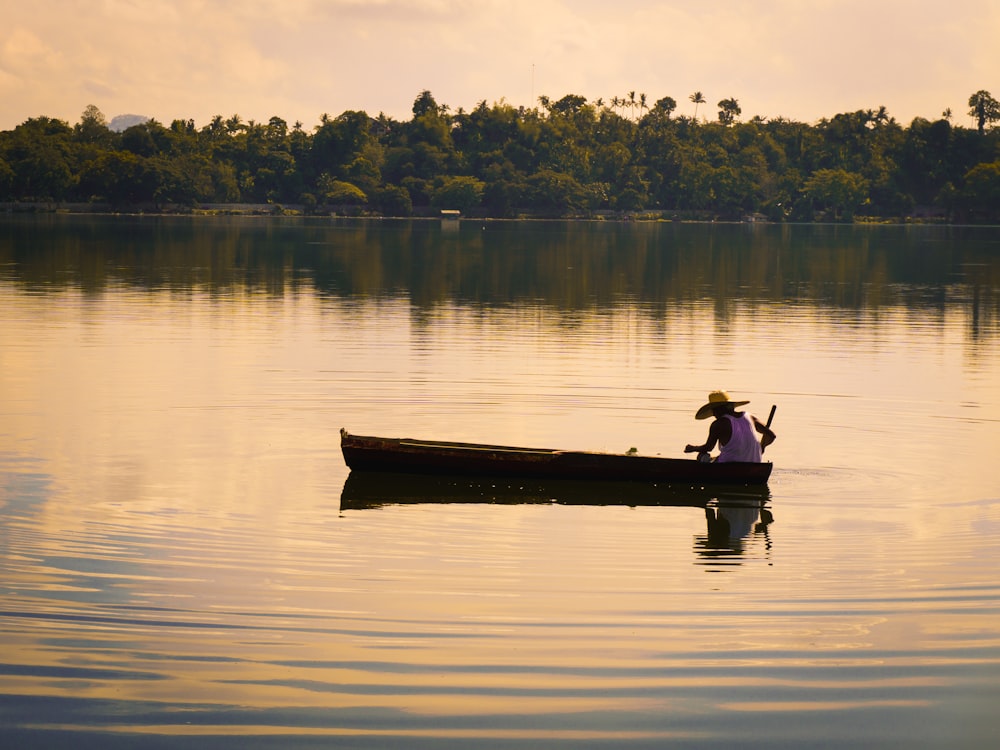 a man in a boat on a lake with trees in the background