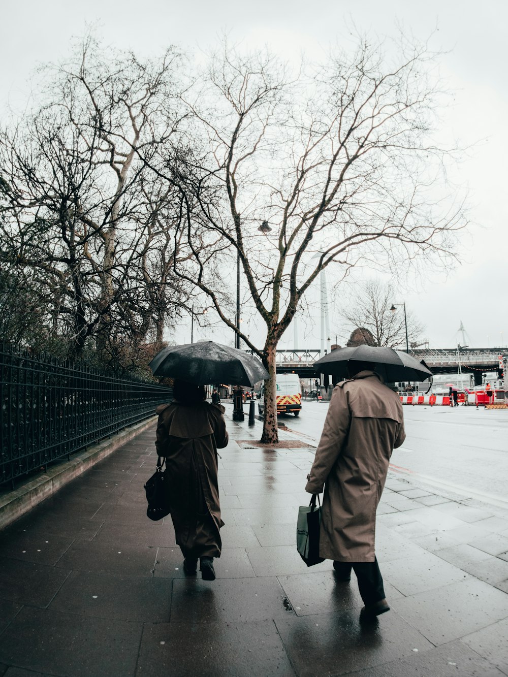 a couple of people walking down a sidewalk with umbrellas