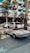 A classic white convertible Mercedes-Benz is parked on a paved driveway in front of a modern hotel with a sign reading 'Jumeirah'. The background features palm trees and a glass building facade, with other parked cars visible nearby.