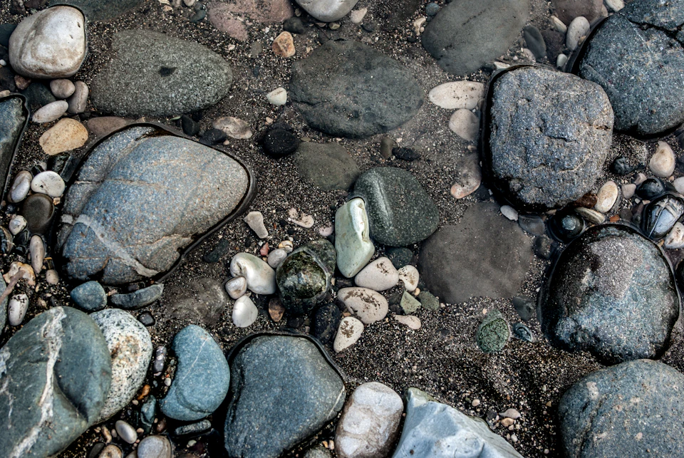 Close-up view of rocky riverbed with scattered pebbles and reflected water surfaces