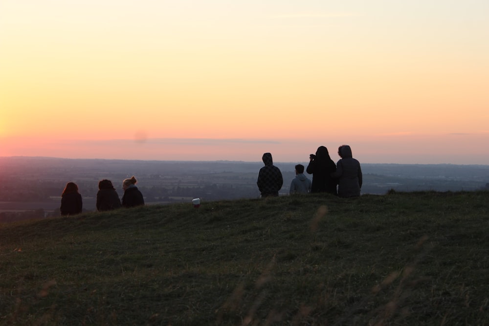 a group of people sitting on top of a grass covered hill