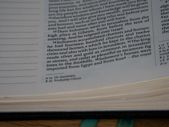The image shows a close-up of a page from a book, specifically a biblical text. The text discusses Solomon accumulating chariots and horses. There are footnotes at the bottom of the page detailing additional information.