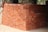 A large stack of red bricks is neatly arranged, forming a rectangular structure. Wooden beams and parts of a building framework are visible in the background. The ground is sandy, indicating an unfinished or construction setting.