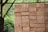 A stack of neatly arranged brown bricks is situated in an outdoor setting with a lush green background. The bricks appear raw and rustic, indicating a construction or industrial site.