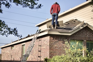 a man standing on the roof of a house preparing the roof by removing the old shingles