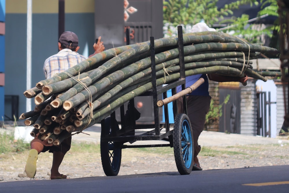 um homem empurrando um carrinho cheio de troncos por uma rua
