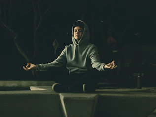 a man in a hoodie meditating in a park at night