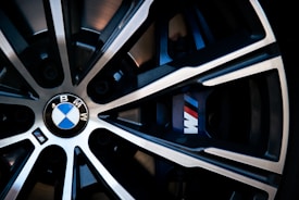 Close-up view of a BMW wheel featuring the emblem in the center and the 'M' logo indicative of the BMW M performance division. The spokes of the wheel are metallic with a combination of black and silver colors, creating a sleek and modern appearance.