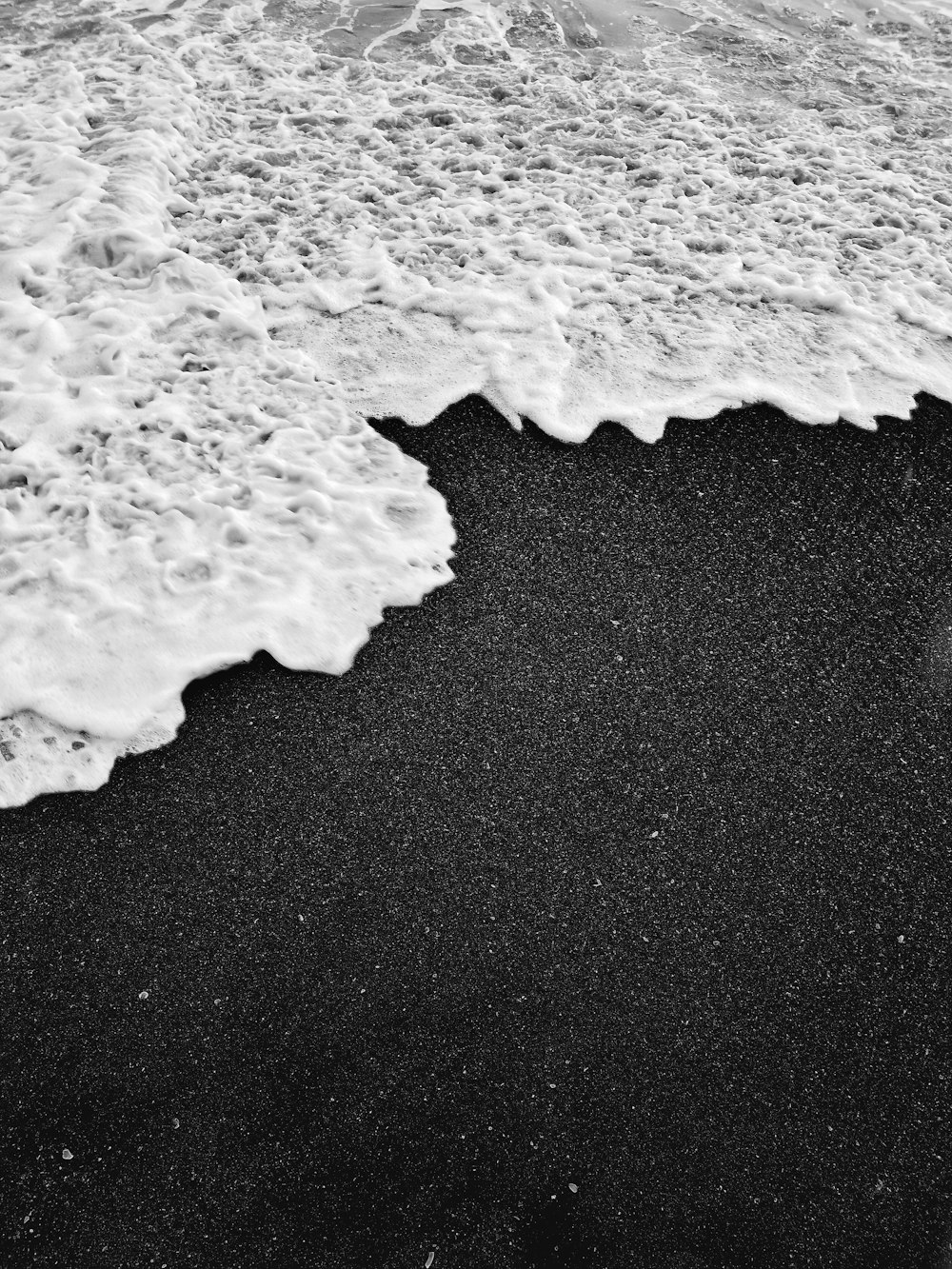 Ein schwarzer Sandstrand mit einer Welle, die hereinkommt