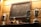 A wooden wall features a framed collection of vintage keys. Below the frame, several decorative objects including two silver trophies, and a series of carved wooden figurines and birds are displayed on a shelf. A modern trophy with a star design is also present.