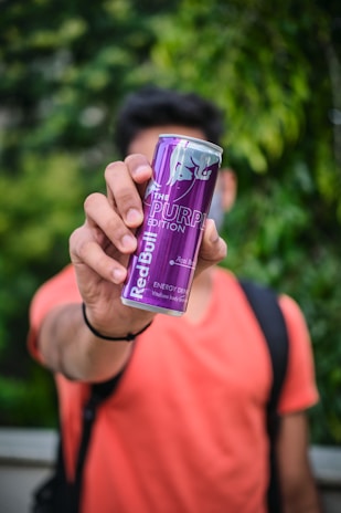A person holding an energy drink can with a bright, outdoor background.