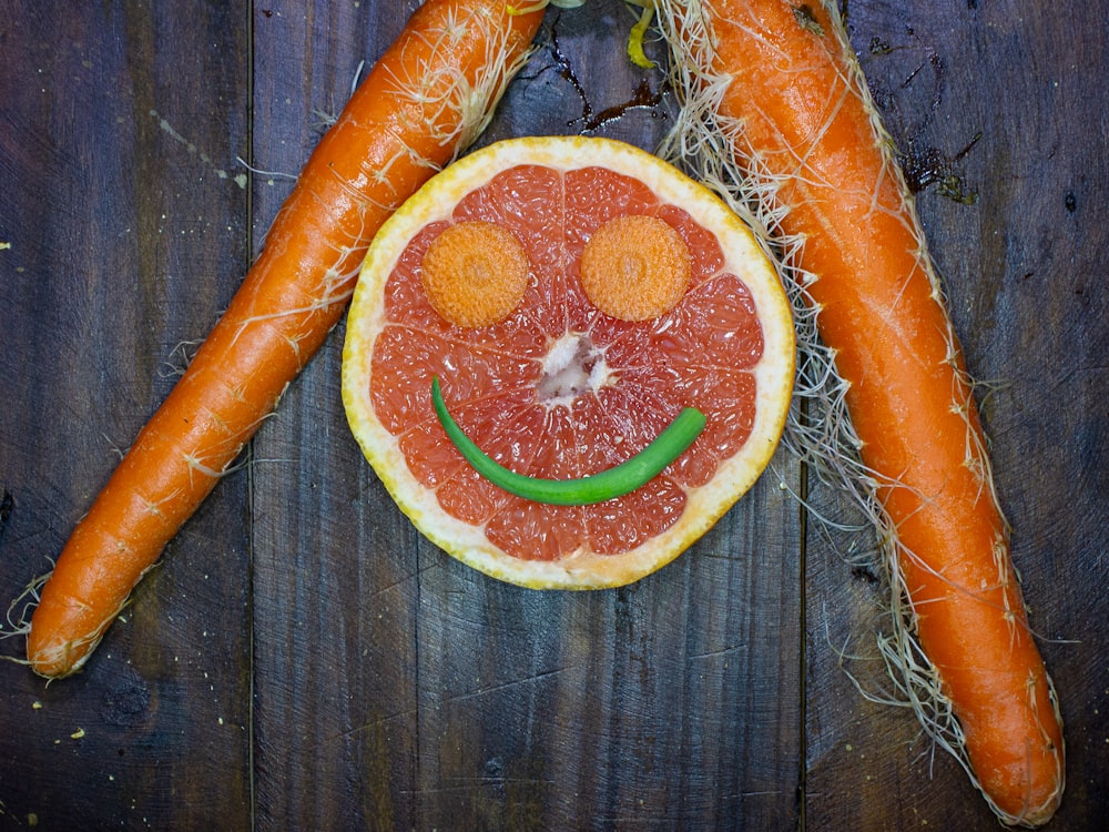 a grapefruit, carrots, and grapefruit smiley face on a