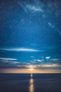A serene night sky filled with twinkling stars and a glowing crescent moon over calm waters.