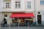 a man riding a bike past a red awning