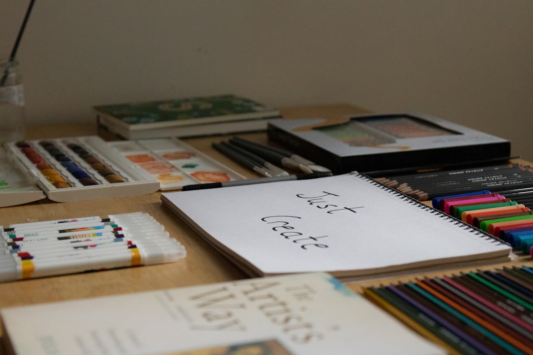a wooden table topped with lots of books and pencils, A table with art materials and a sketchpad with