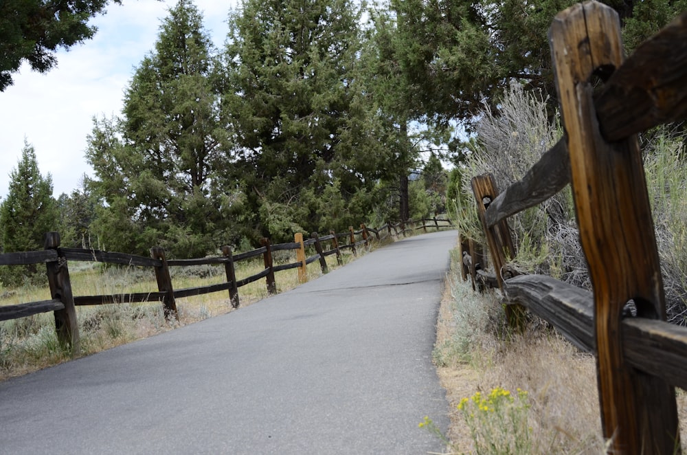 a wooden fence next to a road surrounded by trees