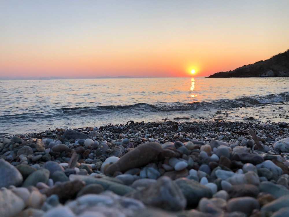 the sun is setting over the ocean on a rocky beach