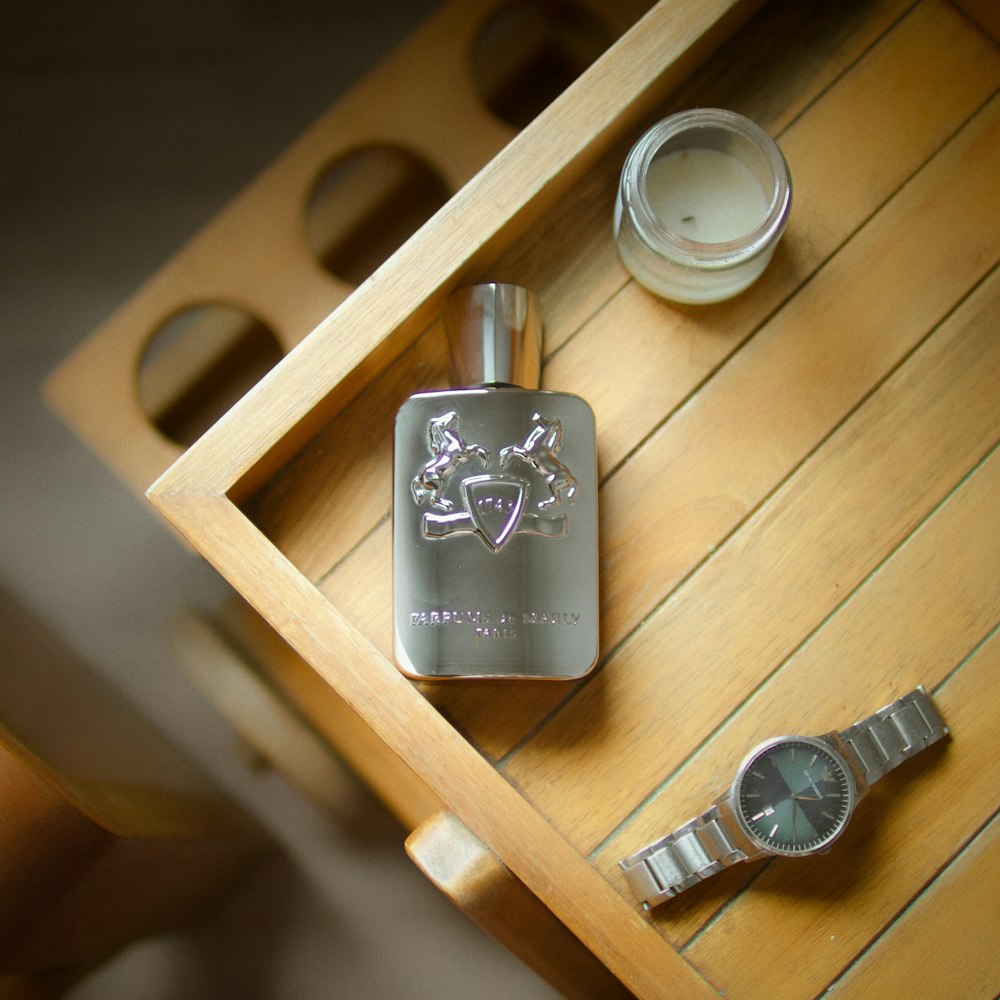 a wooden table topped with a metal flask and a watch