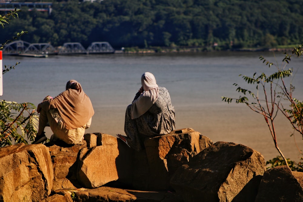 two people sitting on rocks near a body of water