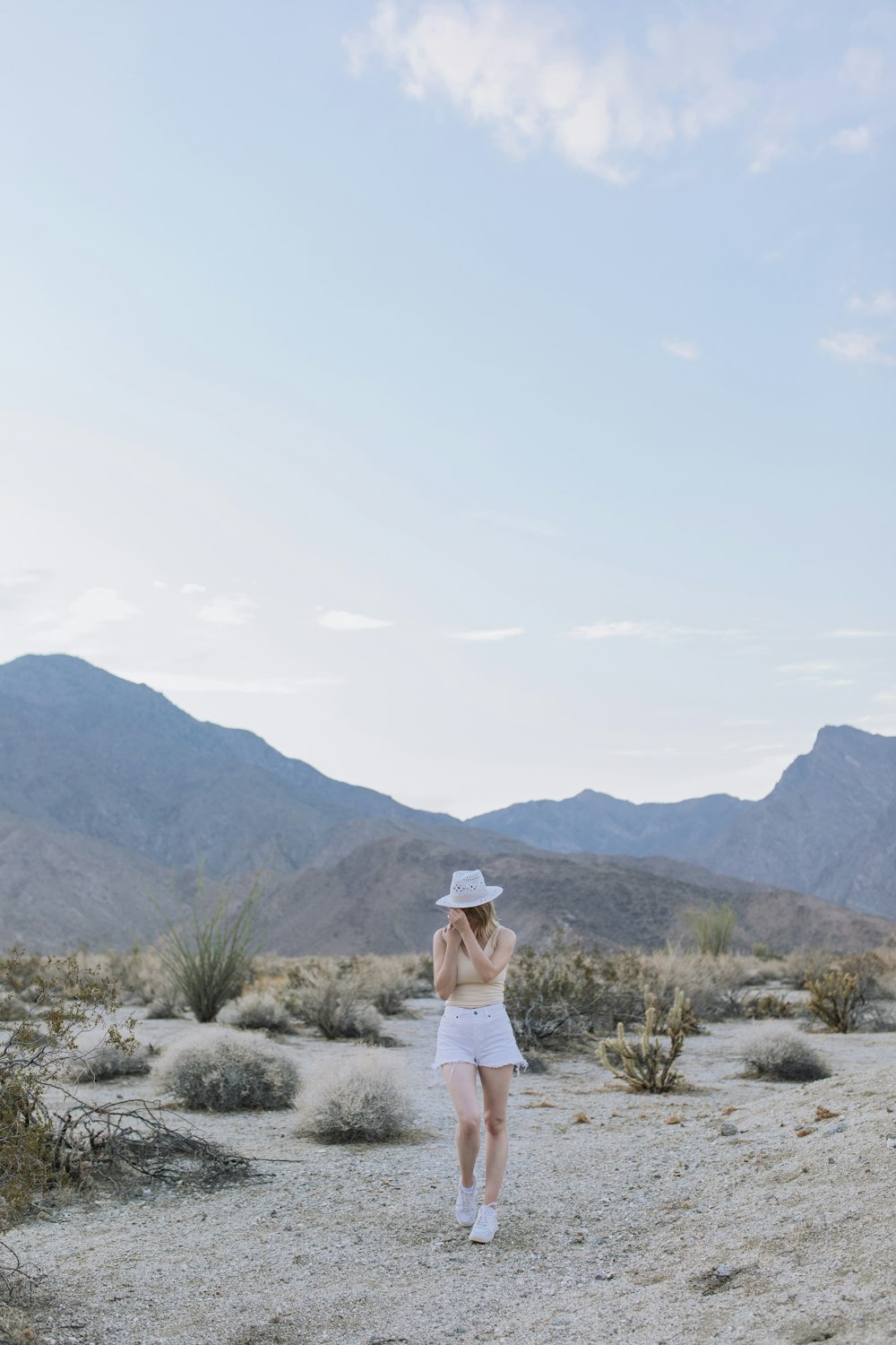 a woman in white shorts and a hat walking in the desert