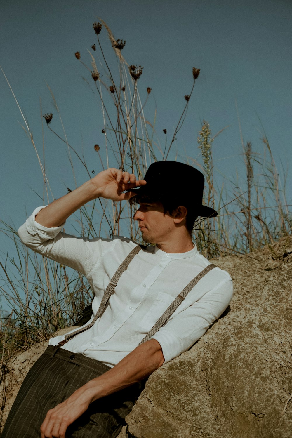 a man sitting on a rock wearing a hat and suspenders