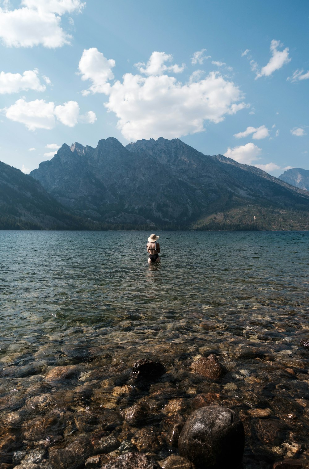 a man wading in a lake with mountains in the background