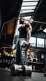Close-up of a muscular man lifting heavy dumbbells in a dimly lit gym.