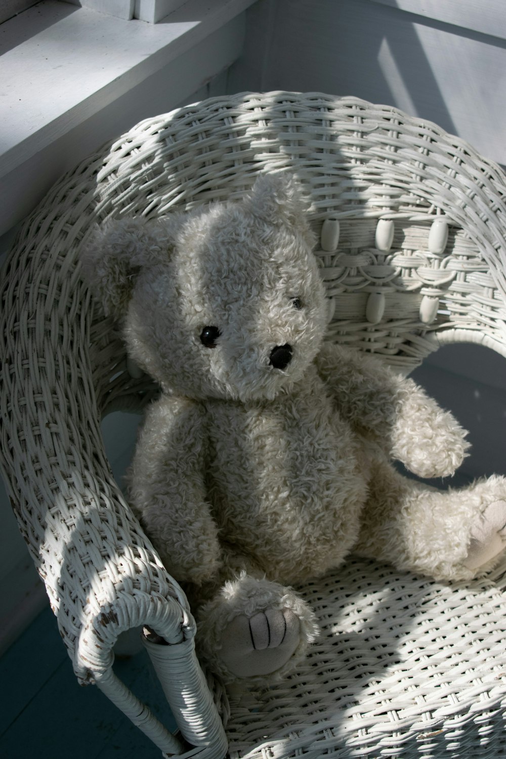 a white teddy bear sitting in a wicker chair