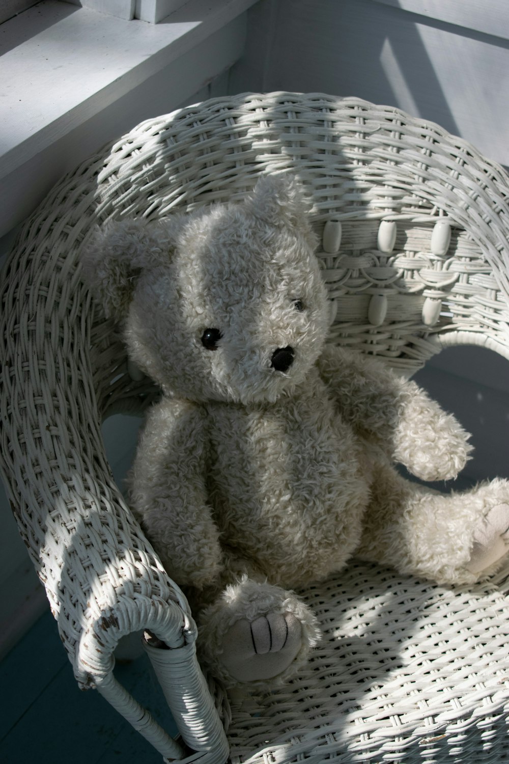 Un oso de peluche blanco sentado en una silla de mimbre