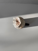A cup of coffee topped with whipped cream and a sprinkle of cocoa powder is placed on a flat surface with a warm light casting shadows.