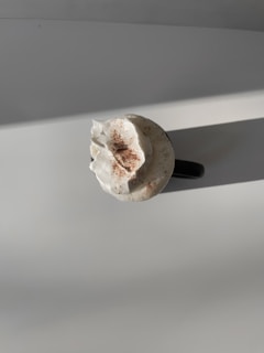 A cup of coffee topped with whipped cream and a sprinkle of cocoa powder is placed on a flat surface with a warm light casting shadows.