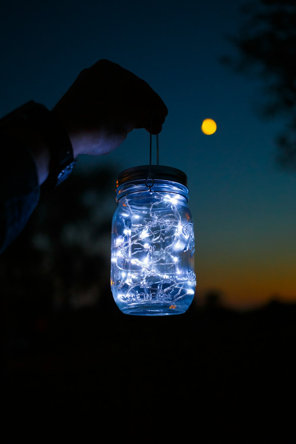 a person holding a mason jar with string lights in it